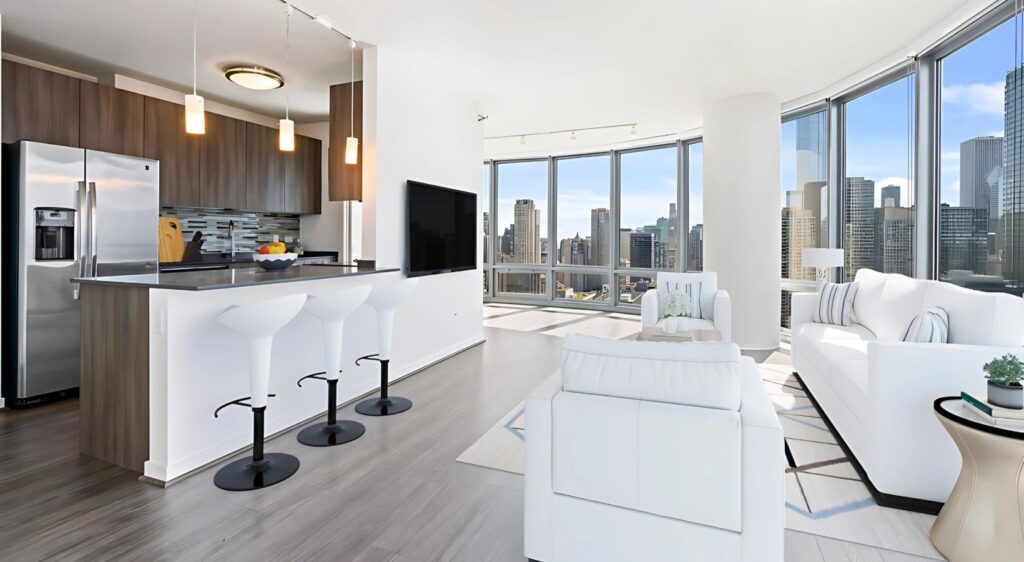 Modern open-concept apartment with floor-to-ceiling windows, city views, a kitchen with bar stools, and a living area with white furniture.