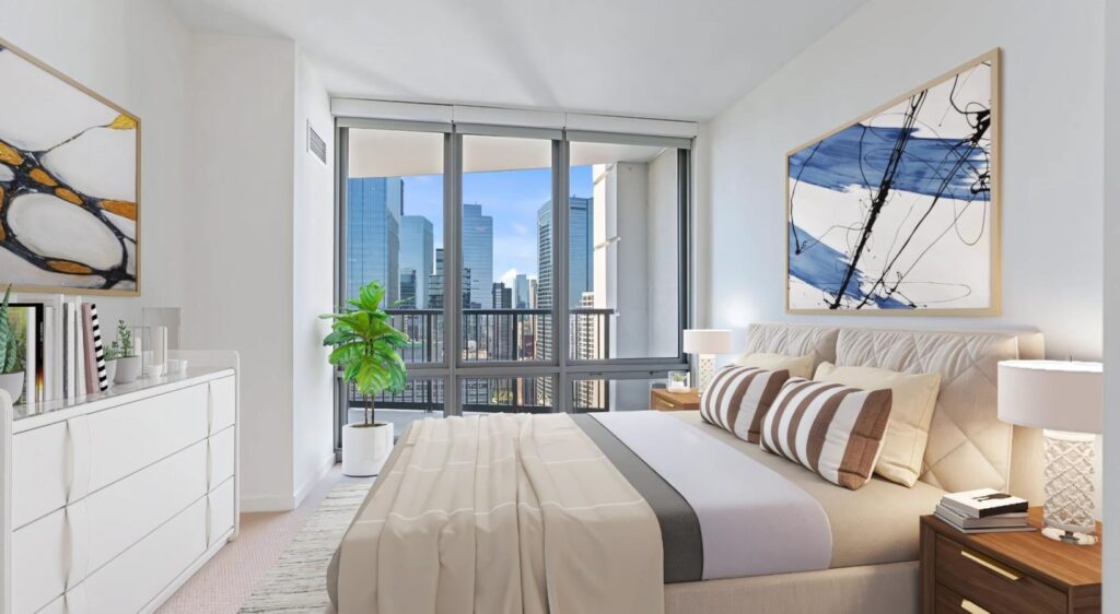 Modern bedroom with large windows overlooking a cityscape, featuring a bed, dresser, abstract artwork, lamps, and a potted plant.