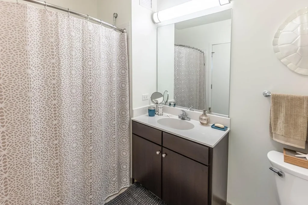 Modern bathroom with a patterned shower curtain, dark wood vanity, large mirror, towel rack, and simple countertop items.