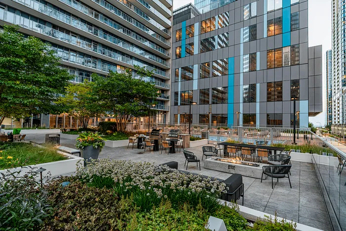 Modern apartment complex courtyard with outdoor seating, fire pits, greenery, and high-rise buildings in the background.