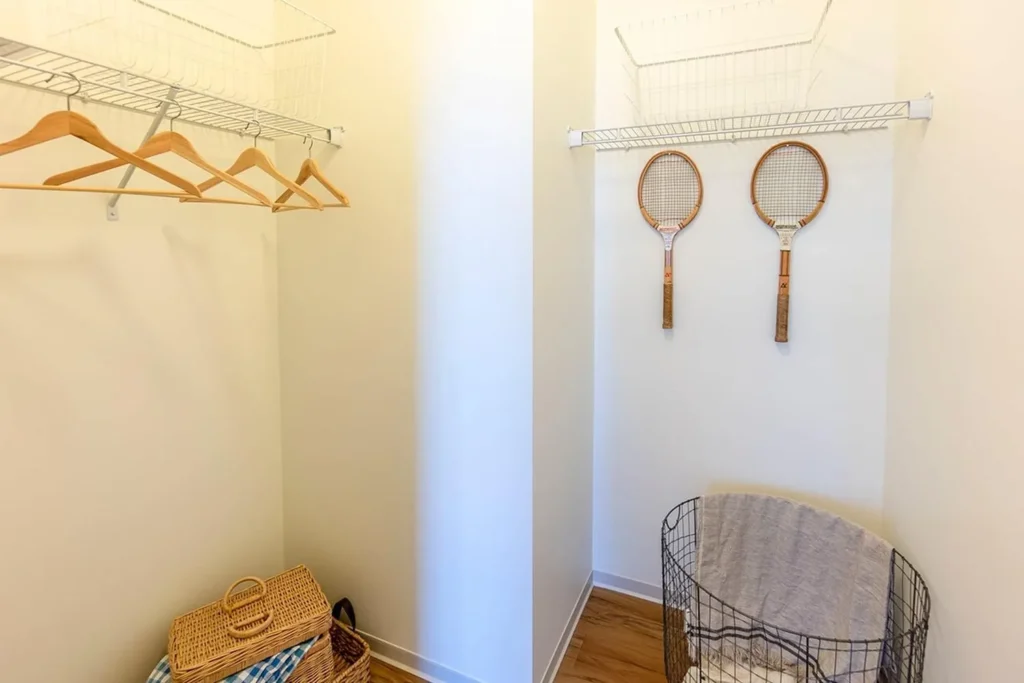 A walk-in closet with several wooden hangers, two tennis rackets hanging on the wall, wire shelves, a wicker basket, and a laundry hamper.