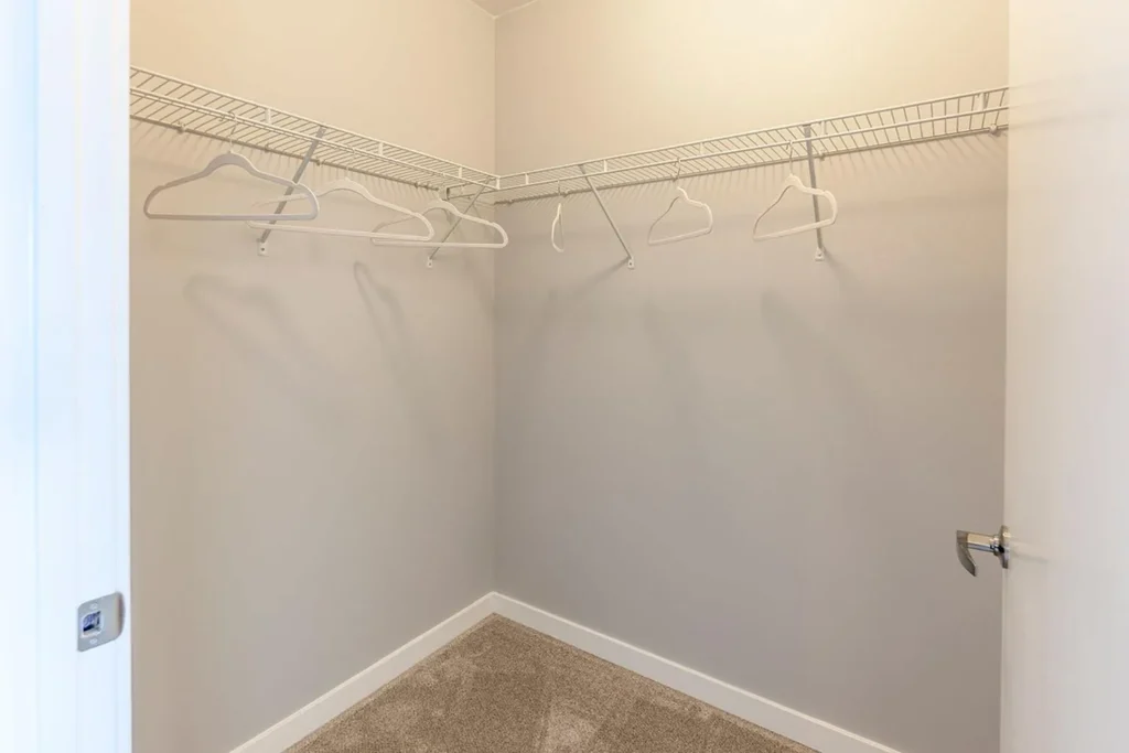 Empty walk-in closet with beige carpet, white walls, a wire shelving unit along two walls, and several empty white hangers.