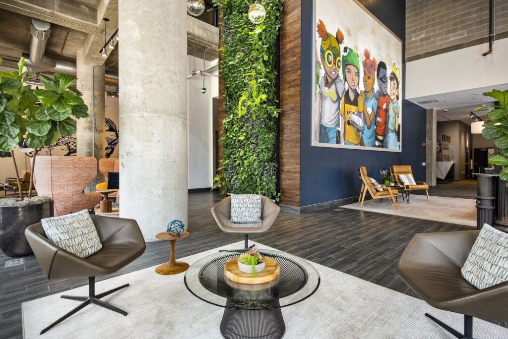 Modern lobby with three chairs around a glass coffee table, a vertical green plant wall, and a large colorful artwork on the wall.