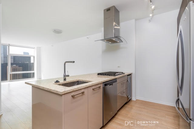 Modern kitchen with a center island, sink, gas cooktop, stainless steel appliances, wood flooring, and large windows providing natural light.
