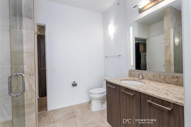 Modern bathroom with a glass shower, toilet, wall-mounted light, and a vanity with a granite countertop and mirror.