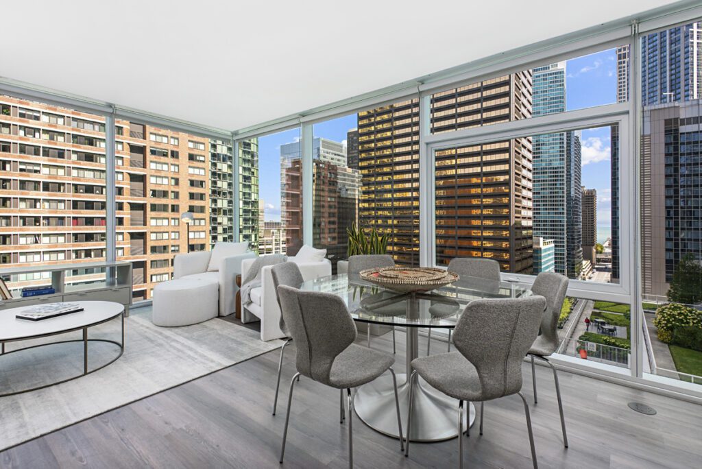Modern high-rise apartment with floor-to-ceiling windows, featuring a dining area and living room with cityscape views and contemporary furnishings.