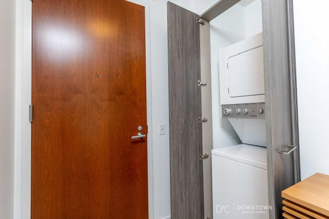 A stacked washer and dryer unit is in a small laundry closet next to a closed wooden door and a partially open gray door.