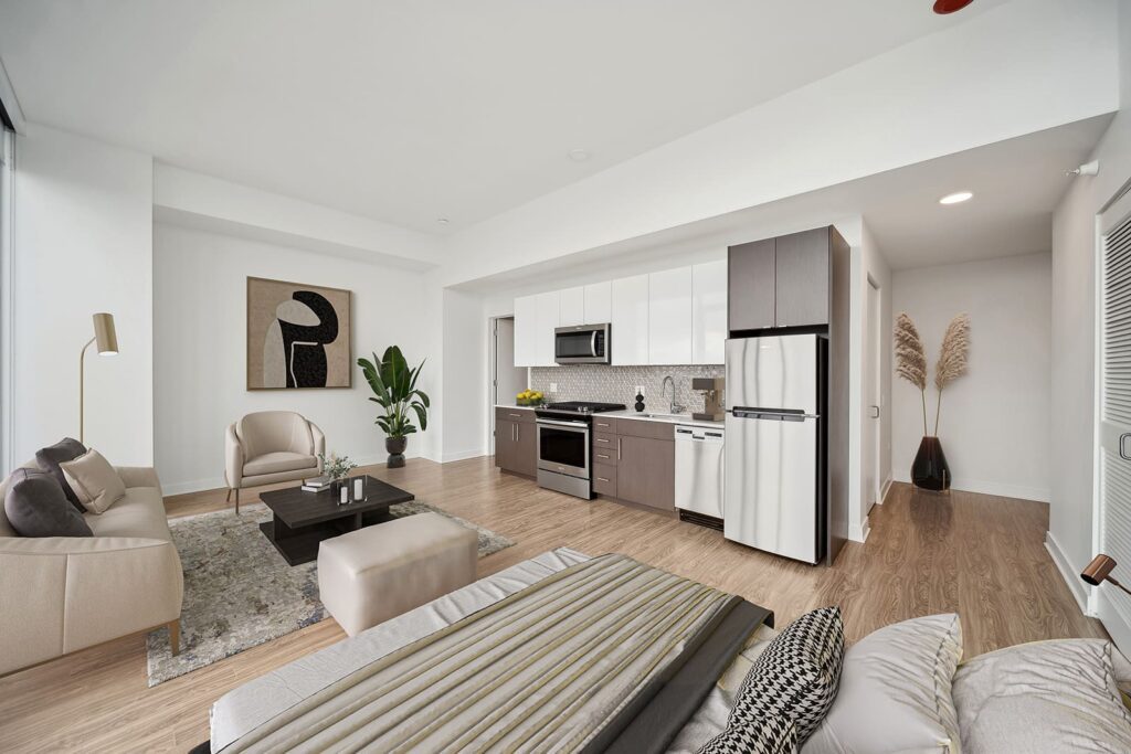 Modern open-plan living room and kitchen with neutral tones, stainless steel appliances, wooden flooring, and contemporary decor including a large abstract painting and indoor plants.