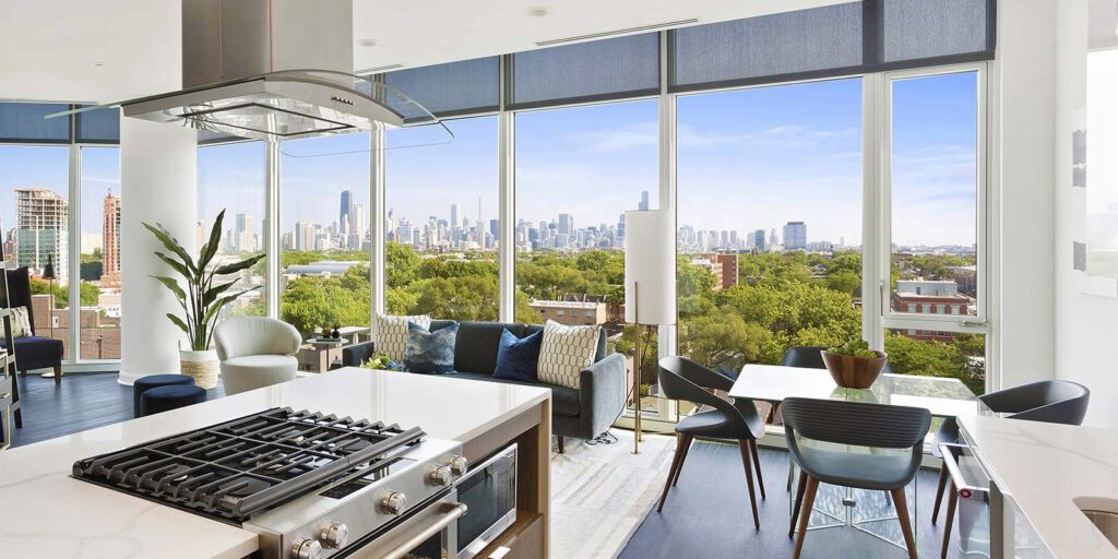 Modern open-concept kitchen and living area with large windows offering a view of a city skyline and green park.