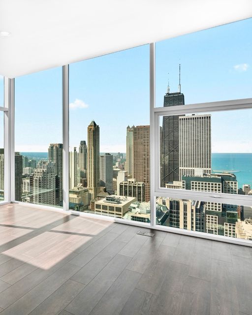 A modern, unfurnished room with floor-to-ceiling windows overlooking a city skyline and Lake Michigan in the background.