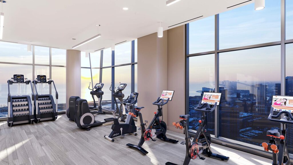 Modern gym with treadmills, stationary bikes, elliptical machines, free weights, and floor-to-ceiling windows overlooking a cityscape at sunset.