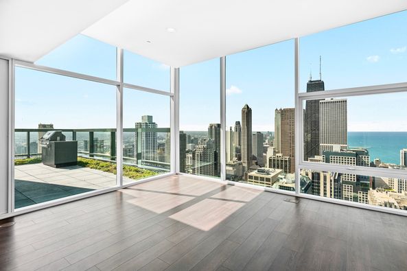 Corner room with large floor-to-ceiling windows overlooking a city skyline and lake, featuring wood flooring and access to a balcony.