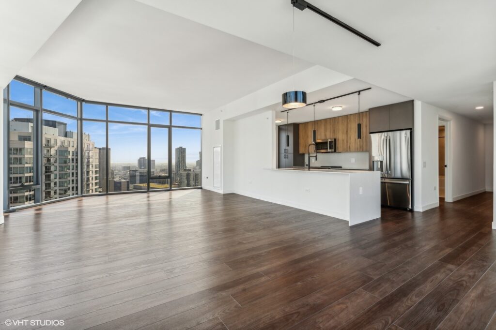 Spacious modern apartment interior with hardwood floors, open kitchen, and large windows offering city skyline views.