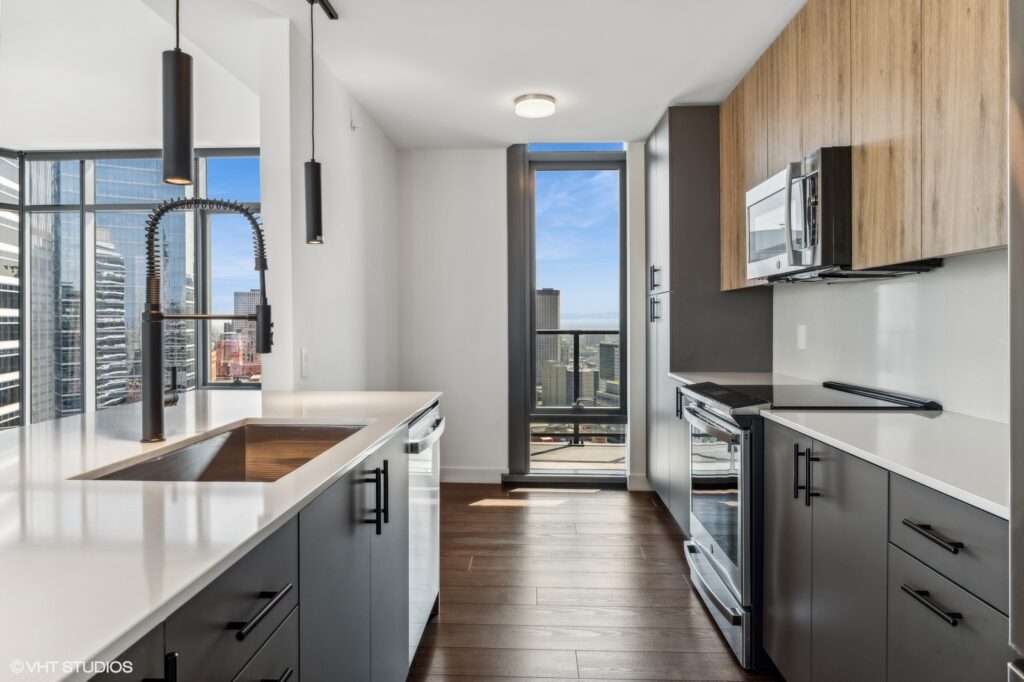 Modern kitchen with dark cabinets, stainless steel appliances, and a large window offering a city view. Light wood floors and a sleek faucet are featured.