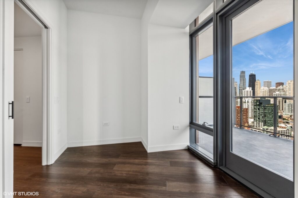 Interior of a room with wooden floor, a large window, and a city skyline view.
