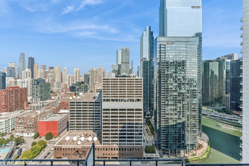 View of a cityscape with tall modern buildings, a river in the foreground, and a clear blue sky.