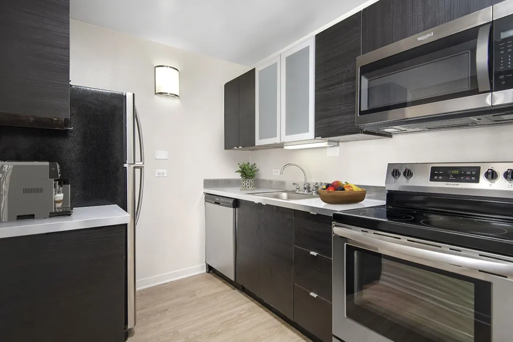 Modern kitchen with dark wood cabinets, stainless steel appliances, a fruit bowl on the counter, and a hardwood floor.