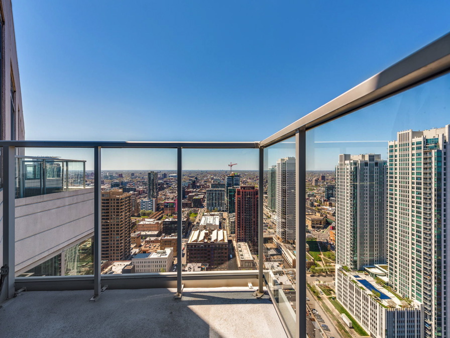 View from a high-rise balcony overlooking a cityscape with tall buildings under a clear blue sky.