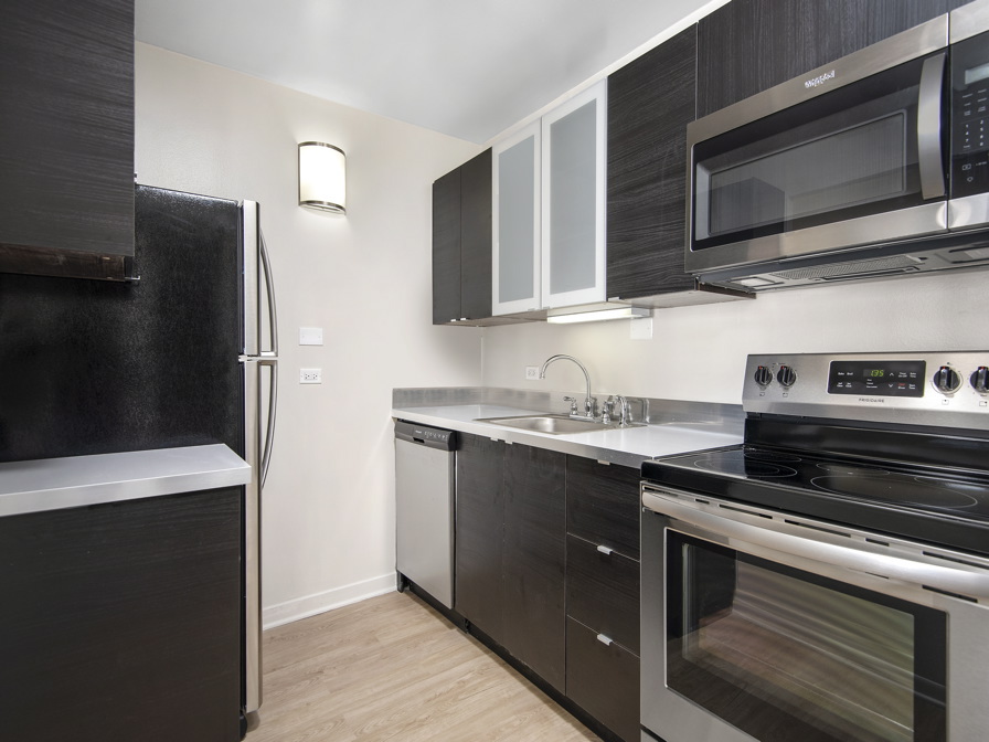 Modern kitchen with dark cabinets, stainless steel appliances, and light wood flooring. Includes a refrigerator, stove, microwave, and dishwasher.
