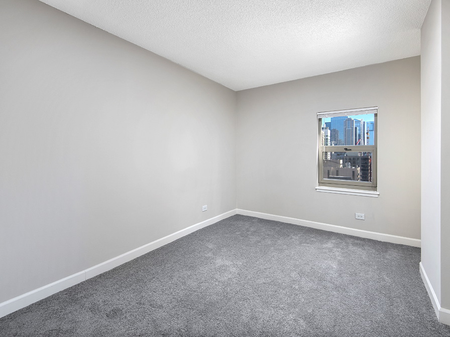Empty room with gray carpet, white walls, and a window showing a cityscape.