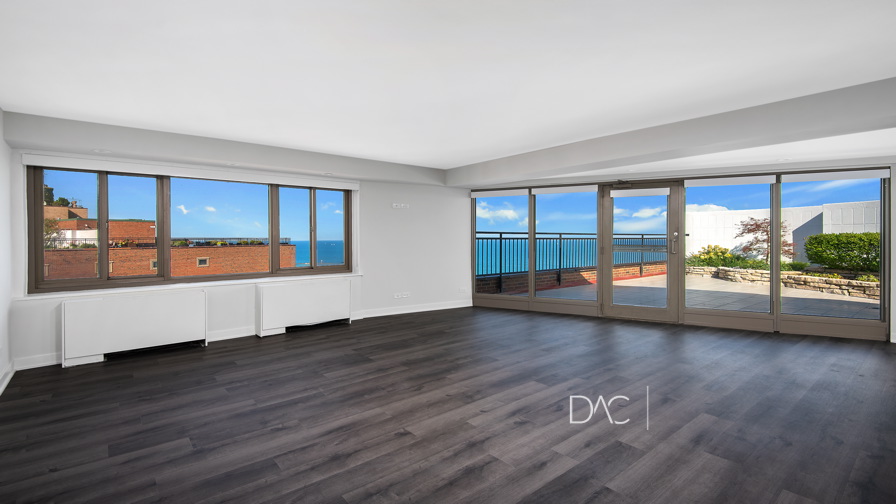 Unfurnished living room with dark wood flooring, large windows, and glass doors opening to a terrace with views of the lake and city buildings.