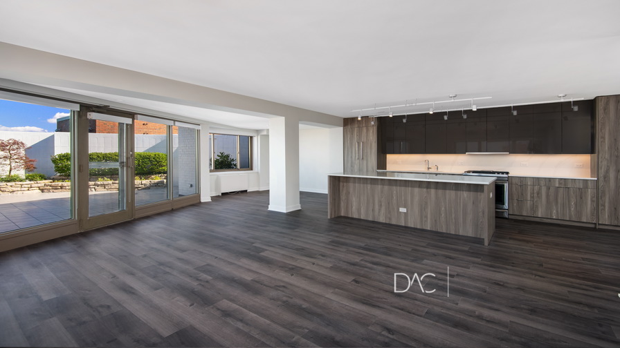 Modern open-plan kitchen and living area with dark wood flooring, large windows, and a sliding door leading to a patio.