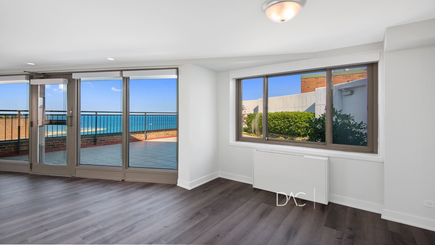 Modern, unfurnished room with large windows, wood flooring, and a view of a balcony overlooking the ocean.