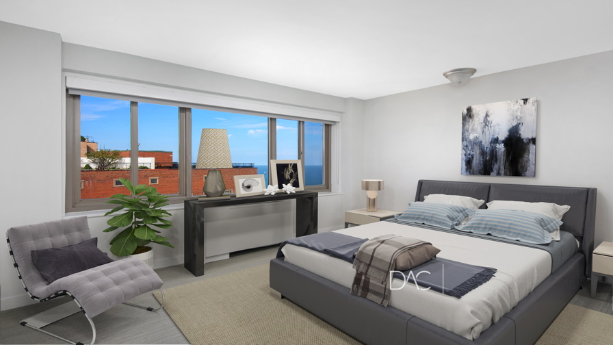Modern bedroom with a gray bed, chair, and console table, large window showing blue sky and buildings, abstract art above the bed, and a potted plant by the window.