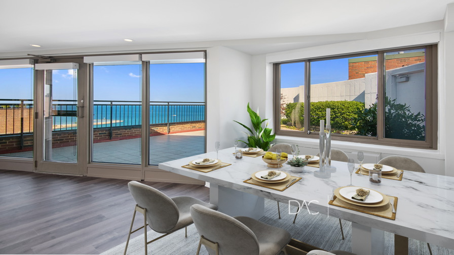 A dining room with a marble table set for six, looking out onto a terrace with a view of the ocean.