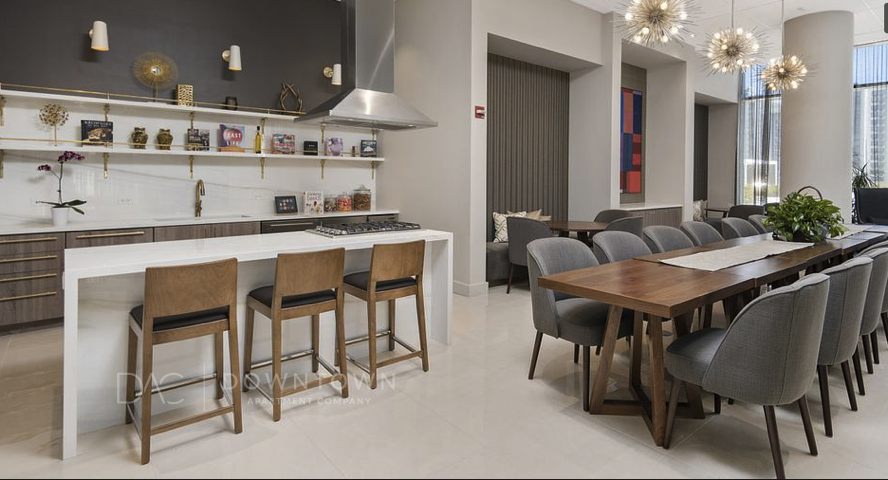 Modern kitchen and dining area with bar stools at a white island, wooden dining table with gray chairs, decorative lighting, and wall accents.