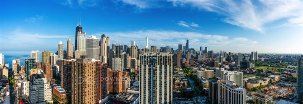 Panoramic view of a city skyline with tall skyscrapers under a clear blue sky and light clouds.