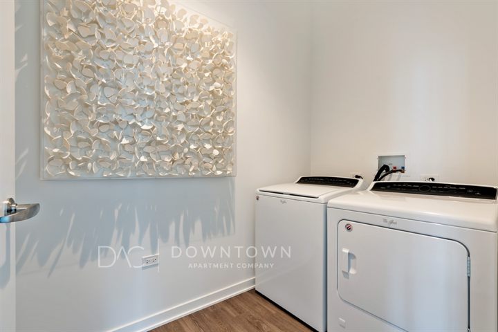 Laundry room with a white washing machine on the left and a dryer on the right. Wall art featuring white textured petals is displayed on the left wall.