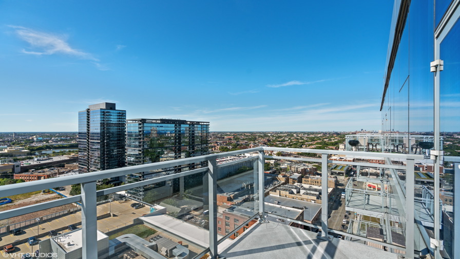View from a balcony of a high-rise building overlooking a cityscape with several buildings and a clear blue sky.