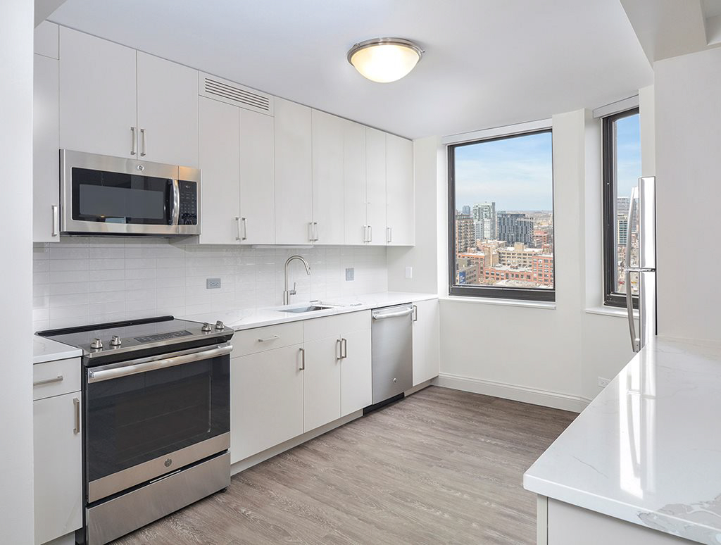 Modern kitchen with white cabinets, stainless steel appliances, and hardwood floor. Large window offers a city view.