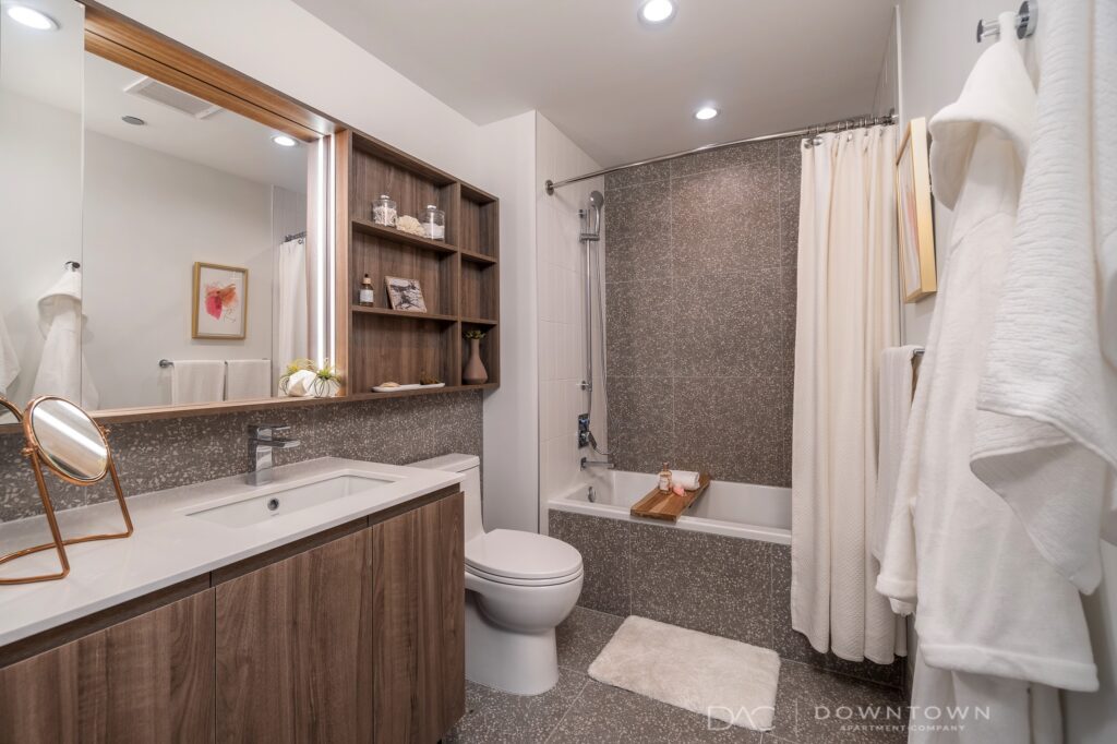 Modern bathroom with wood cabinetry, white sink, and granite countertop. Bathtub with a shower curtain, towels on the wall, and a decorative shelf.