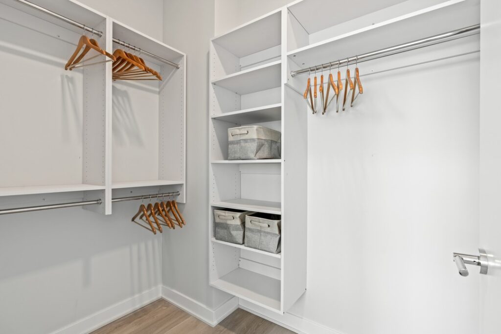 An empty white walk-in closet with wooden hangers on rods, and fabric storage bins on shelves. The closet has light hardwood flooring and an open door.