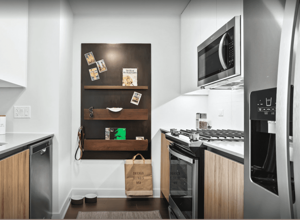 Modern kitchen with stainless steel appliances, wooden cabinets, and a black wall organizer. A grocery bag and pet bowls are on the floor.