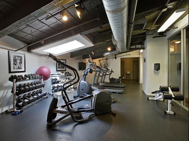 Gym room with exercise equipment, including elliptical machines, dumbbells on racks, a red exercise ball, and a bench under a skylight.