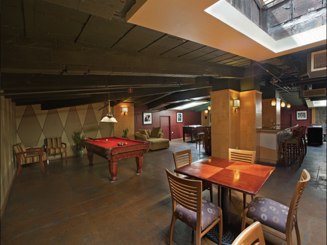A spacious room with a billiards table, seating area, and a bar. Ceiling features exposed beams and skylights.