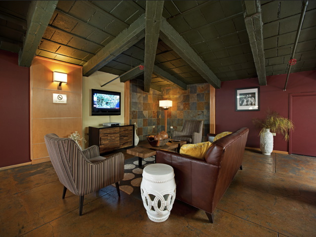 Lounge area with wooden ceiling, leather sofa, striped chairs, TV, and decorative elements like stools and vases, set against a warm-toned wall with artwork.