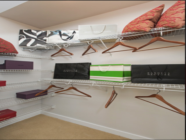 Walk-in closet with wire shelving holds colorful shopping bags, wooden hangers, and decorative pillows.