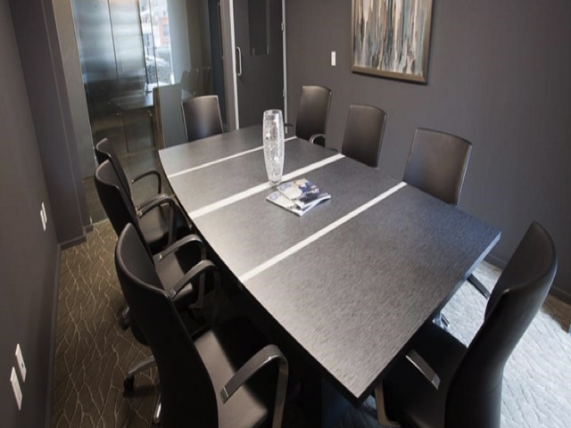 A sleek, modern conference room with a dark table, eight chairs, a decorative vase, and a magazine. Neutral walls, abstract art, and a glass door complete the setting.