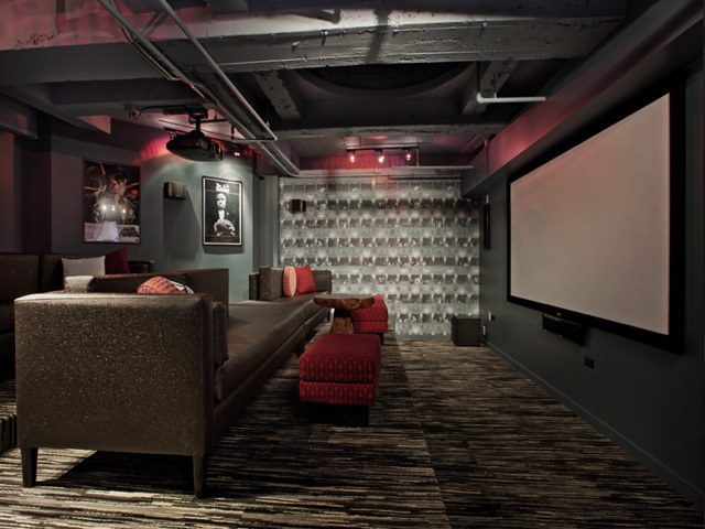 Home theater with a large screen, couches, and red lighting. Walls display framed artwork. Carpeted floor and ceiling with exposed beams.