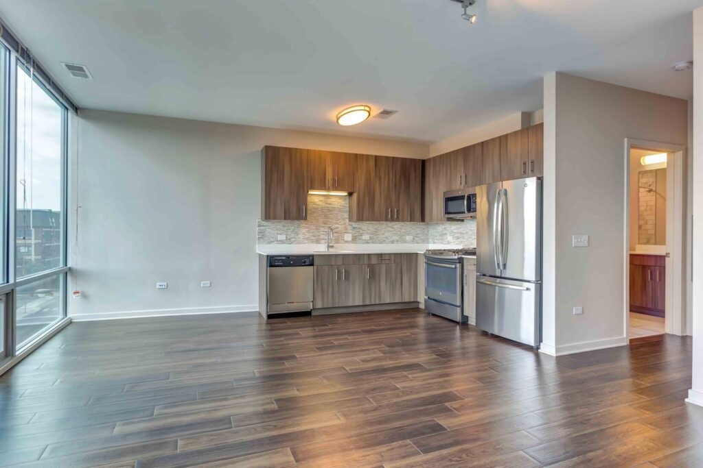 Modern kitchen with stainless steel appliances, wood cabinetry, and a tiled backsplash. Hardwood floors and large windows provide natural light to the space.