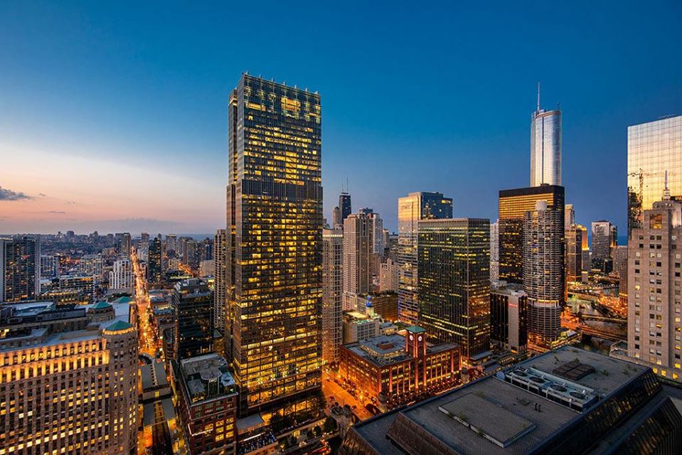 City skyline at dusk with illuminated skyscrapers and a clear sky.
