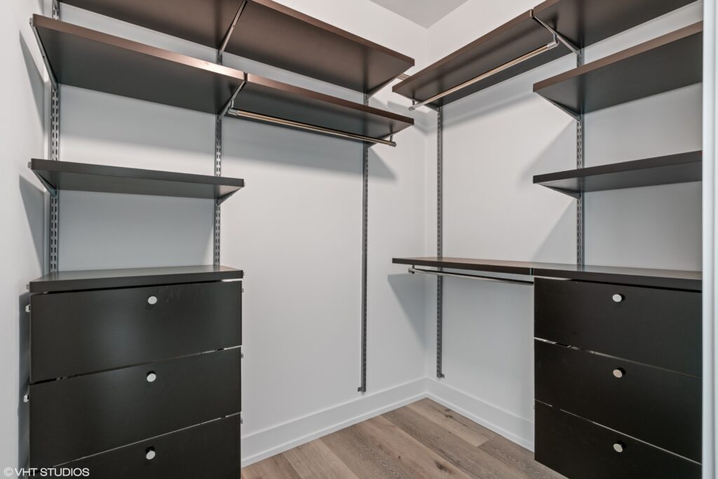 A modern walk-in closet with black shelving, drawers, and hanging rods, set against white walls and a wood-patterned floor.