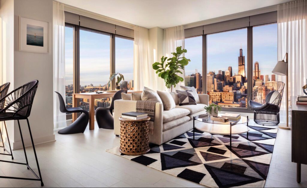 Modern living room with large windows showcasing a city skyline. Features a beige sofa, geometric rug, potted plant, and dining table with black chairs. Natural light fills the space.