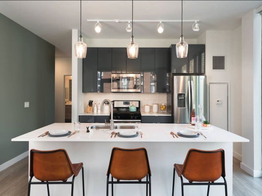 Modern kitchen with white island, three brown stools, pendant lights, and stainless steel appliances. Green and white walls complete the space.