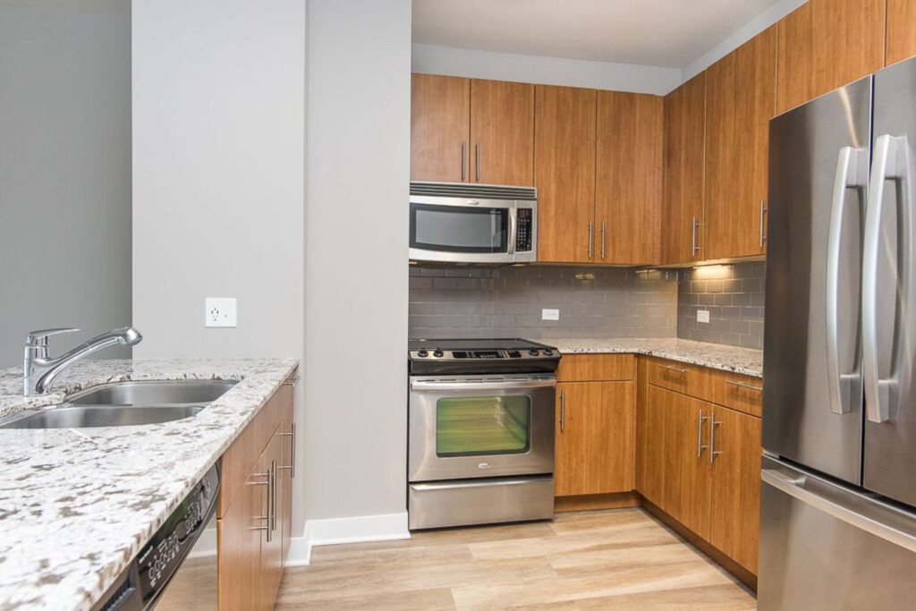Modern kitchen with stainless steel appliances, wooden cabinets, marble countertops, and a dual-basin sink.