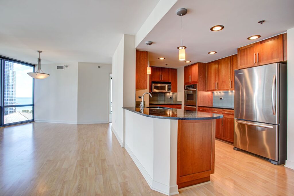 Modern open-plan kitchen and living area with wooden floors, stainless steel appliances, and large windows offering a view of the cityscape and water.